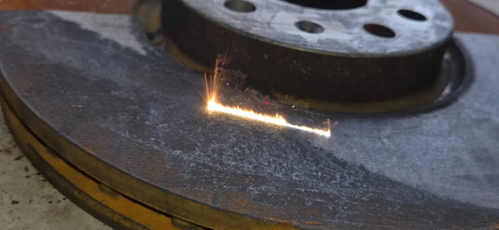 Décapage laser en cours sur un disque de frein : ligne d'ablation, étincelles et acier remis à nu